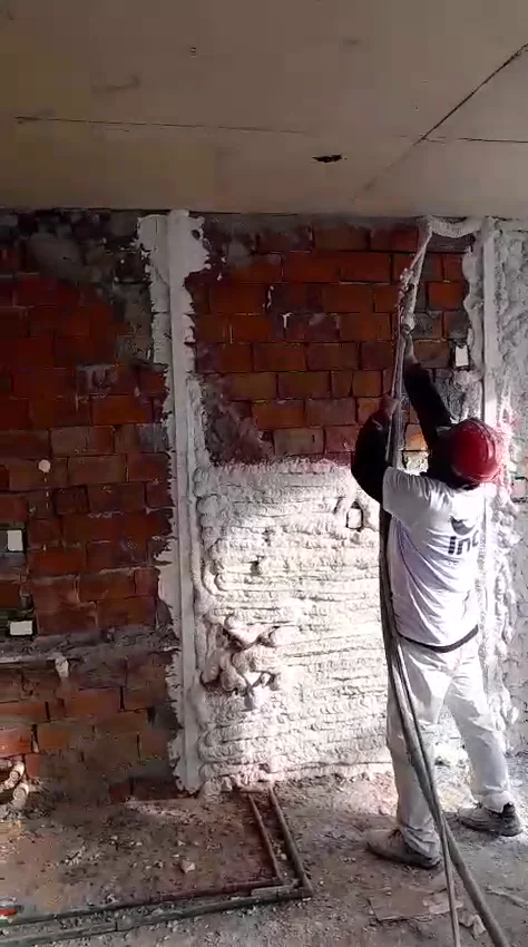 Operario proyectando yeso con máquina sobre pared de ladrillo
